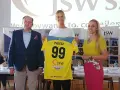 Trzy osoby pozują z koszulką z numerem 99 i nazwiskiem PIELESZ. W tle logo JSW i napisy związane z firmą, być może z okazji wydarzenia w MTS Żory.
