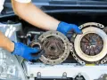 Mechanik w niebieskich rękawiczkach trzyma części sprzęgła. Zastanawiasz się, ile trwa wymiana sprzęgła?