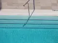 Escalera metálica en piscina de agua clara, con marcas de profundidad. El mantenimiento de piscinas es clave para su disfrute.