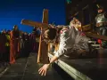 Scena drogi krzyżowej: Jezus w cierniowej koronie, z krwią na szacie, upada pod ciężarem krzyża. Tłum widzów obserwuje to poruszające przedstawienie.