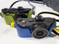 Dwie stylowe Leica X2 w kolorowych futerałach: jedna zielona, druga niebieska. Idealne do uchwycenia każdej chwili.