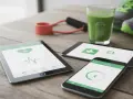 Na stole leżą tablet i smartfon z aplikacją do uzależnień, pokazującą puls i aktywność. Obok zielony koktajl, gumy do ćwiczeń i buty sportowe.
