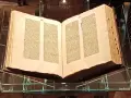 Otwarta biblia gutenberga pelplin, prezentowana na szklanym stojaku, świadectwo historii druku.
