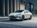 Biały sedan BYD Seal 6 DM-i jedzie po miejskiej ulicy.