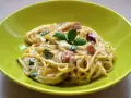 Spaghetti carbonara ze śmietaną, podane w zielonej misce, udekorowane bazylią. Pyszny przepis na klasyczne danie.