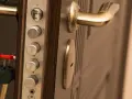 Poignée de porte blindée avec plusieurs serrures et une clé rouge. Des marques sur le cylindre supérieur suggèrent une tentative d'effraction.
