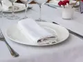 Une table dressée avec une assiette blanche, une serviette de table pliée, une fourchette et un couteau. La dimension serviette de table est parfaite pour cette présentation élégante.