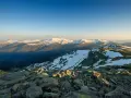Paisaje montañoso nevado al amanecer, con rocas en primer plano y el pico Madrid en la distancia.