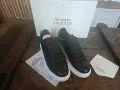 Czarne sneakersy Alexander McQueen na grubej, białej podeszwie, obok pudełka z logo marki.