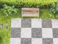 Ideas de suelo para terraza: un banco de madera sobre césped y un patrón de tablero de ajedrez de guijarros blancos y grises.