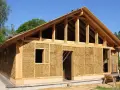 Construction d'une maison en paille écologique, avec une structure en bois visible et des murs isolés en bottes de paille.