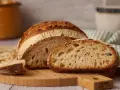 Ein frisch gebackenes reines Emmerbrot, aufgeschnitten auf einem Holzbrett. Die Krume ist luftig und goldbraun.