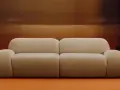 Divano beige bouclé, un materiale morbido e accogliente, con tavolini neri e lampade cromate.