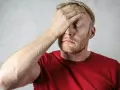 Uomo con mano sulla fronte, occhi chiusi, espressione di stress. Possibili sintomi di attacchi epilettici da stress.