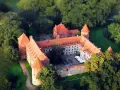 Zamek w Bytowie otoczony zielenią, z czerwonymi dachami i kamiennymi murami, wygląda jak z bajki.