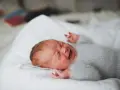 Noworodek w szarym sweterku ma niespokojny sen. Jego twarz wykrzywiona jest w grymasie, a rączki unoszą się w powietrzu.