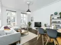 Elegante salón con sofá gris, mesa de centro y comedor. El **suelo oscuro** de madera contrasta con las paredes blancas y la luz natural.