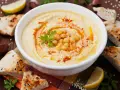 Un bol de houmous maison, garni de pois chiches, de persil et de paprika, servi avec du pain pita, du citron et de l'ail.