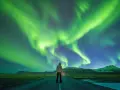 Człowiek stoi na drodze pod rozgwieżdżonym niebem, gdzie tańczy zorza polarna. Islandia, październik, pogoda idealna na takie widowisko.