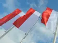 Trzy powiewające na wietrze flagi, każda z czerwono-białą szarfą, na tle błękitnego nieba z chmurami.
