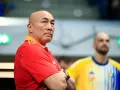 Skupiony trener Vive Kielce w czerwonej koszulce z pomarańczowym kołnierzem, z rękami skrzyżowanymi na piersi.