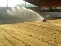 Arrosage d'une carrière équestre par un système mobile, créant un voile d'eau sur le sable.