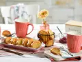 Leckeres Zwieback-Rezept: goldbraune Scheiben auf rosa Platte, dazu Marmelade, Butterdose und rote Tassen.