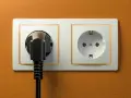 Dwa gniazdka elektryczne na pomarańczowej ścianie. Jedno z nich jest puste, drugie z wtyczką. Zastanawiasz się, jakie gniazdka w Egipcie?