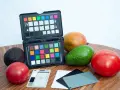 Na drewnianym blacie leżą owoce: awokado, mango, pomidory. Obok znajduje się otwarty colorchecker z kolorowymi polami i szara karta do kalibracji balansu bieli.