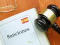 Martillo de juez sobre libro abierto con la palabra "Sanciones" y la bandera de España. Podría ser una multa hacienda.