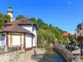Urokliwy strumyk w Polanicy Zdrój, otoczony kamiennymi murkami i zielenią. W tle widać wieżę kościelną i kolorowe kamieniczki.