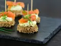 Eleganckie przystawki na komunię: krążki ciemnego pieczywa z kremowym serkiem, łososiem i koperkiem.