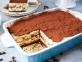 Ein köstliches Tiramisu rezept ohne alkohol, bestäubt mit Kakao, in einer blauen Auflaufform. Ein Stück ist bereits entnommen.