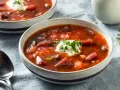 Dwie miseczki aromatycznej zupy z botwiny na mięsie, ozdobione kleksem śmietany i posiekaną natką pietruszki.