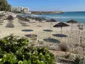 Puste cypr plaże z rzędami parasoli i hotel w tle. Słońce rzuca długie cienie na piasek.