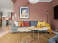 Przytulny salon z szarą kanapą, ozdobioną poduszkami w pastelowe kolory. Na stoliku owoce, a na ścianie obraz.