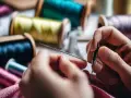 Des mains expertes montrent comment enfiler une aiguille, entourées de bobines de fil colorées.
