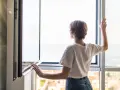 Frau stellt das Fenster ein, um frische Luft hereinzulassen.