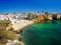 Słoneczna Portugalia w listopadzie: plaża pełna ludzi, białe domy na klifie i turkusowe morze. Idealna pogoda na wakacje.