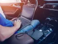Mężczyzna w samochodzie podłącza laptopa do zasilania, pokazując, jak podłączyć komputer do samochodu.