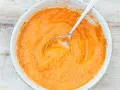 Eine Schüssel mit cremiger, orangefarbener mojo rojo Sauce, die mit einem Löffel umgerührt wird.