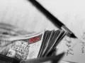 Stos banknotów 100 zł w portfelu, obok długopis i dokumenty. Może to być umowa, gdzie kara umowna jest zapisana.