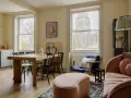 Idee soggiorno piccolo con divano rosa e tavolo in legno. Arredamento accogliente con sedie nere e pouf bombato.
