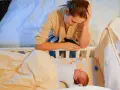 Zmęczona mama pochyla się nad łóżeczkiem, zastanawiając się, kiedy nastąpi regres snu. Niemowlę śpi spokojnie.
