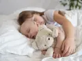Dzieci śpią wtulone w misia. Starsza siostra czuwa nad maluszkiem, pokazując, ile śpi dwulatek i jak ważny jest sen dla rozwoju.