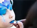 Ein Kind wird mit blauem Lidschatten und Schneeflocken bemalt, um wie Elsa auszusehen. Das Schminken ist leicht und zaubert ein magisches Wintergesicht.