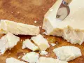 Kawałki Grana Padano na drewnianej desce, gotowe do posypania makaronu lub dodania do sosów.