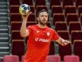 Mateusz Przybylski w czerwonej koszulce z orłem i logo PGNiG, gotowy do rzutu piłką ręczną.