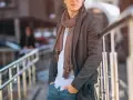 Uomo con cappotto grigio, camicia azzurra e pashmina marrone, un esempio di come indossare una pashmina in modo chic.