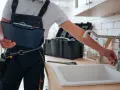 Instrukcja jak zmienić uszczelkę w kranie: hydraulik z narzędziami i teczką przy zlewie.